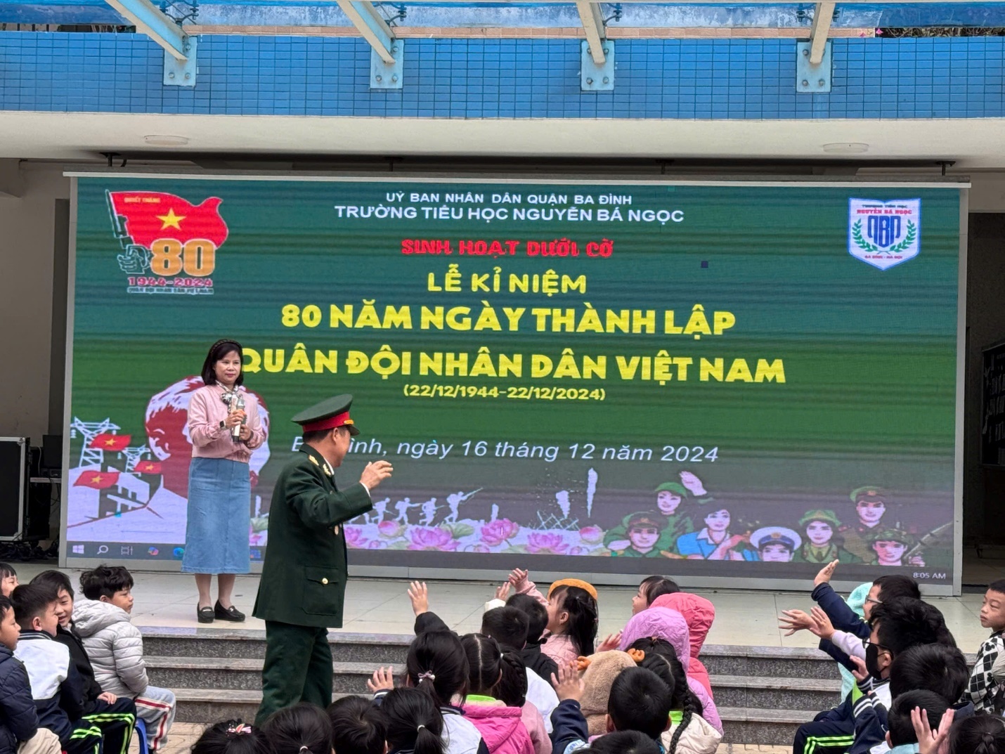 A person in uniform standing in front of a large screen with a group of people

Description automatically generated